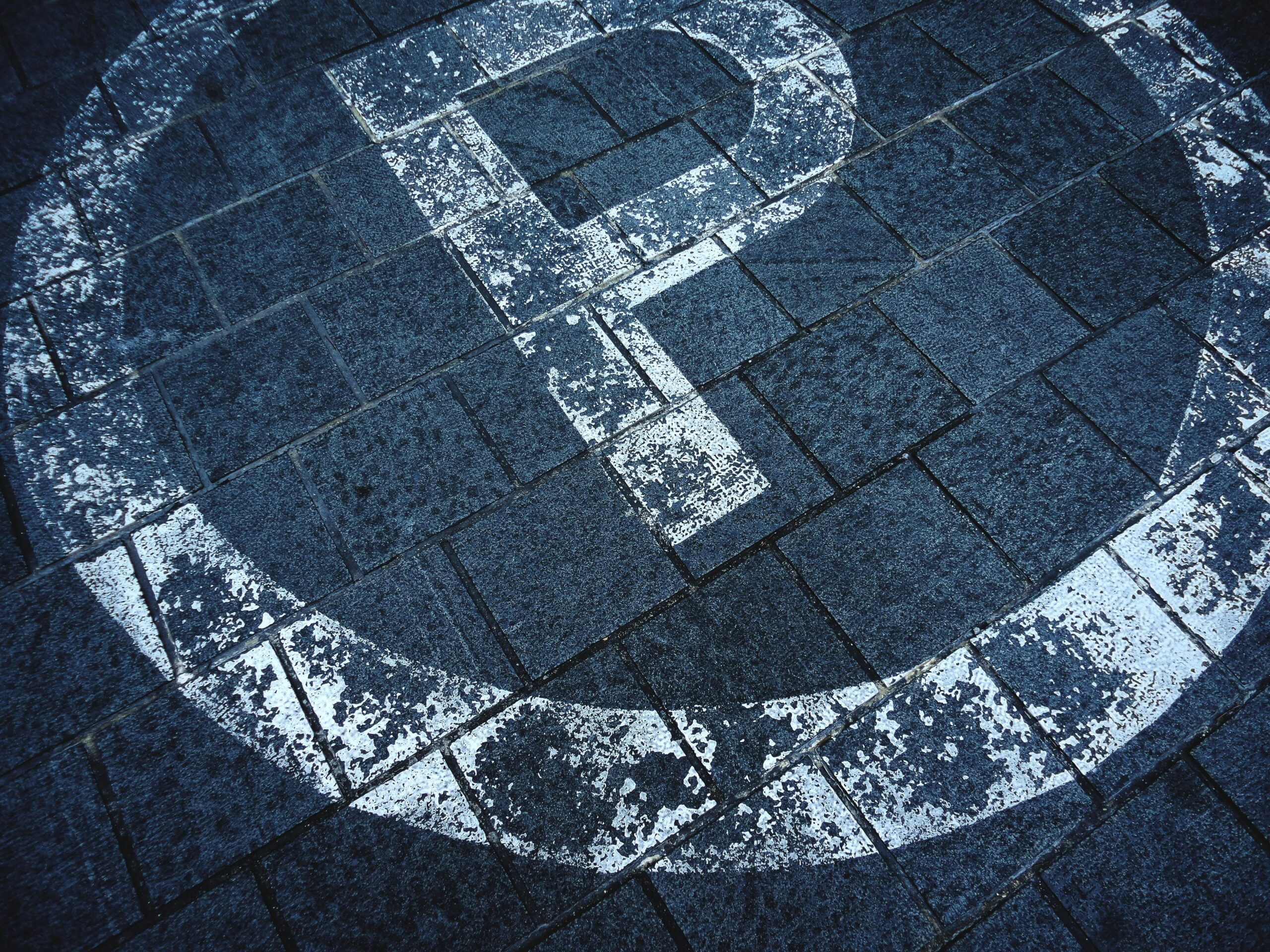 A detailed view of a weathered parking sign on a brick pavement in an outdoor setting.